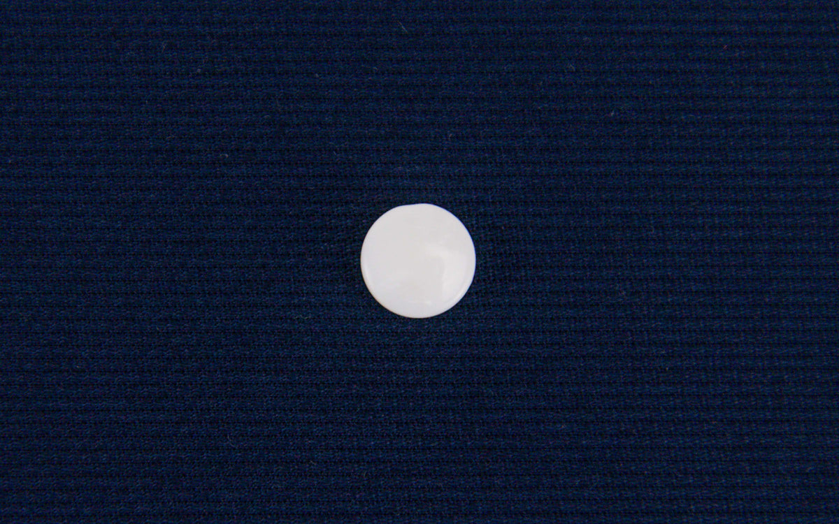 Round white mother of pearl shank button on navy blue fabric background