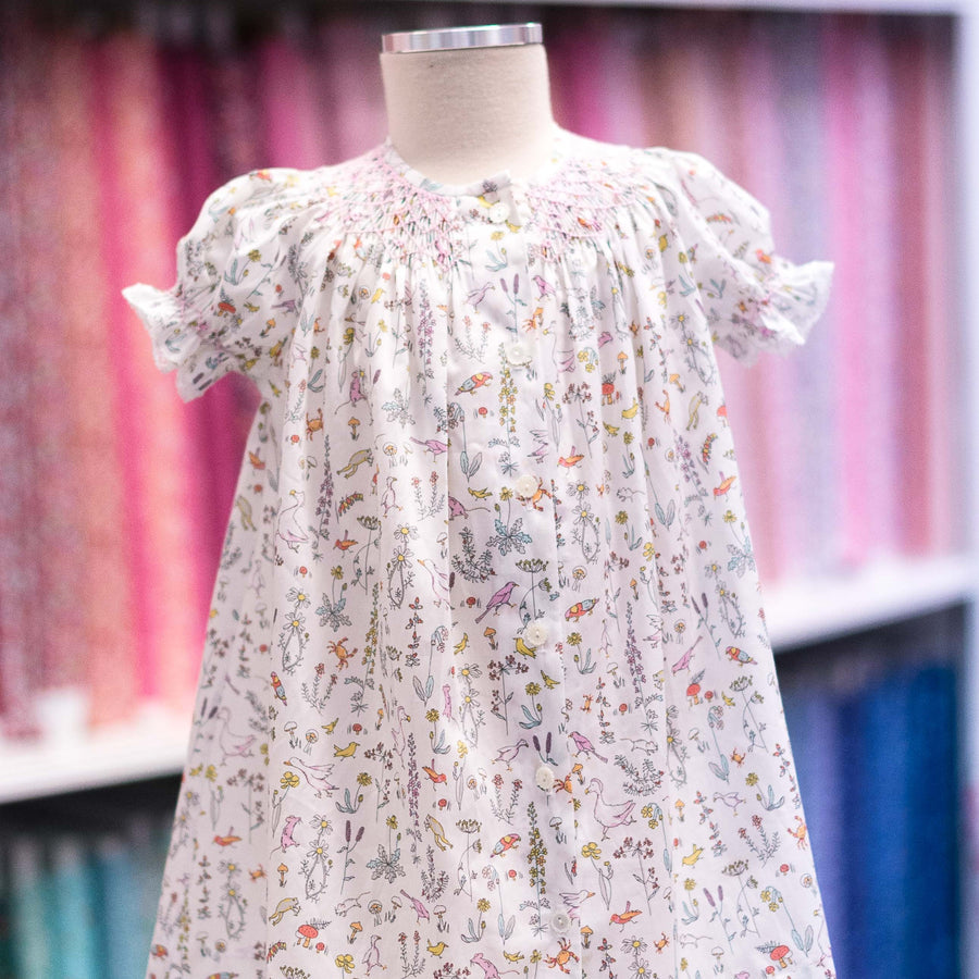 Child's smocked bishop dress in white Liberty Theo A fabric with colorful birds and botanicals
