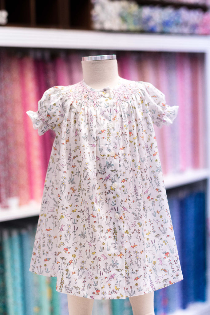 Child's smocked dress in white Liberty Theo A fabric with colorful birds and botanicals print