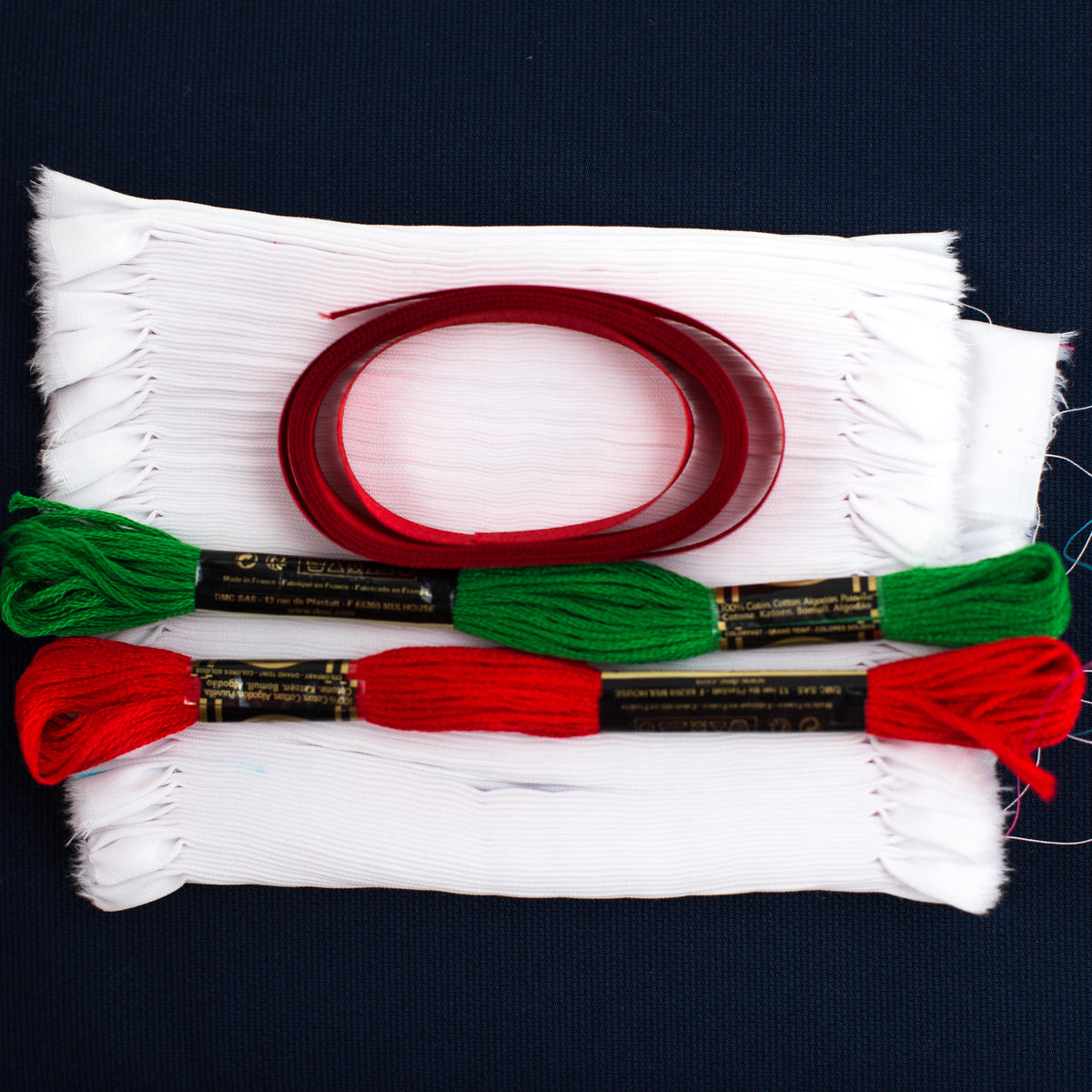 White fabric, red ribbon, green and red DMC embroidery floss skeins for smocked ornament kit